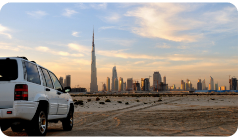 Photo of a car driving through the sand with the skyline of the city of Dubai in the background.